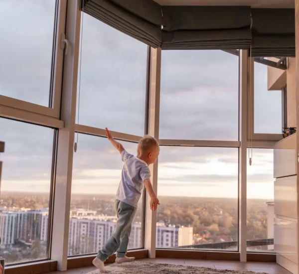 A young child playing near a large window, with a city view outside.